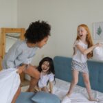 cheerful girls fighting with pillows on bed